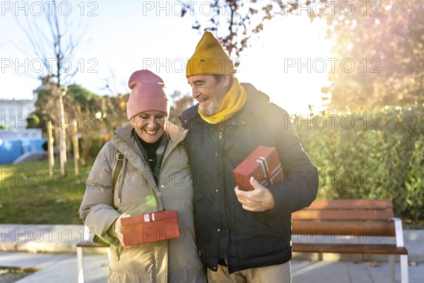 Smiling senior couple exchanging christmas gifts while walking in a city park during a sunny winter day