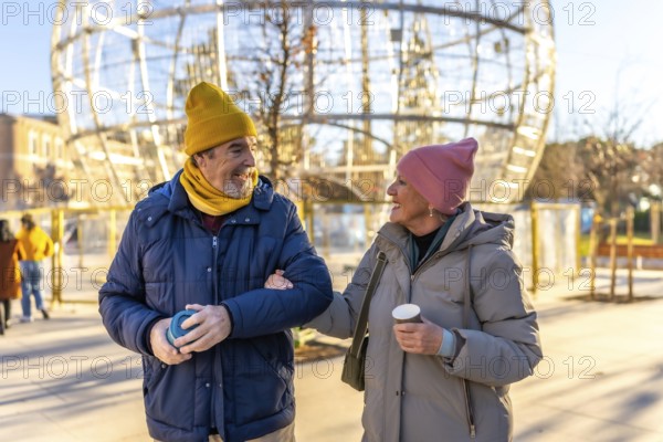 Smiling senior couple walking arm in arm in a city during winter, enjoying a warm beverage and the christmas decorations
