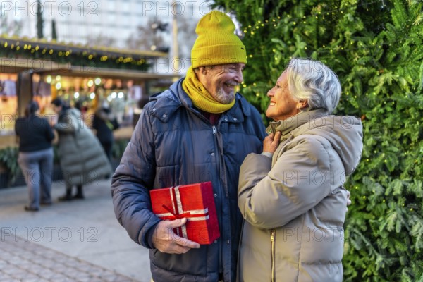 Loving senior couple exchanging christmas gifts at a festive outdoor market, enjoying the holiday spirit together