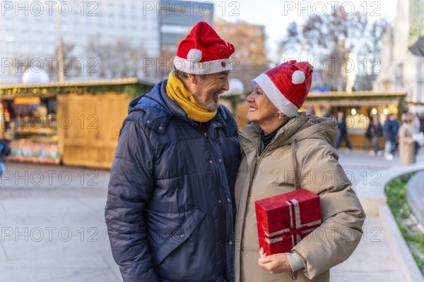 Loving senior couple wearing santa hats exchanging christmas gifts at a christmas market in the city