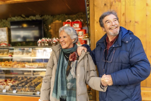 Smiling senior couple holding hands and visiting a traditional christmas market, enjoying winter holidays together