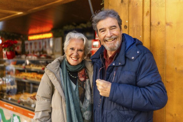 Cheerful retired couple enjoying christmas market during winter holidays, buying presents and tasting local food