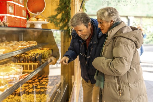 Elderly couple pointing and choosing delicious pastries from a market stall display during the christmas holidays