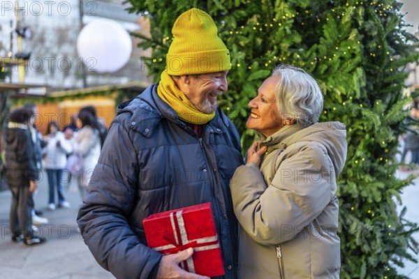 Elderly man surprising his wife with a christmas present at a christmas market during winter holidays