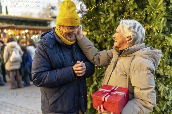Loving senior couple exchanging christmas gifts at a traditional christmas market, enjoying festive atmosphere and sharing precious moments
