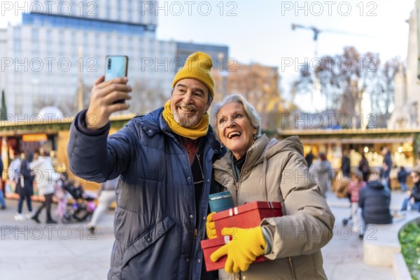 Cheerful senior couple taking a selfie with smartphone at a christmas market, holding gifts and enjoying winter holidays