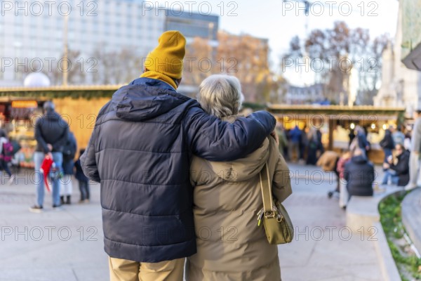 Elderly couple hugging at outdoor christmas market in european city during winter holidays