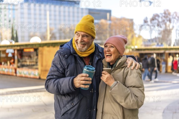 Smiling senior couple enjoying hot drinks at an outdoor christmas market, embracing the festive spirit