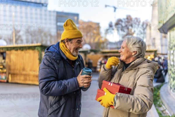 Elderly couple exchanging christmas presents and enjoying a hot beverage at a traditional christmas market during winter holidays