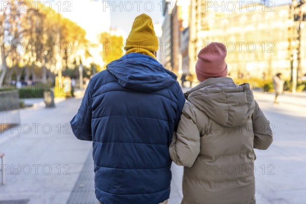 Elderly couple wearing winter clothes and colorful beanies enjoying a walk in a city park during wintertime