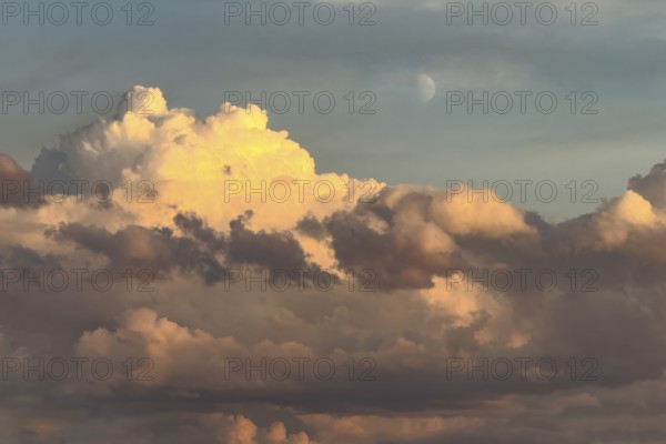 Cumulus cluster clouds are bathed in warm light as dusk falls, illuminated in the background at the top of the sky Hlbmond, international