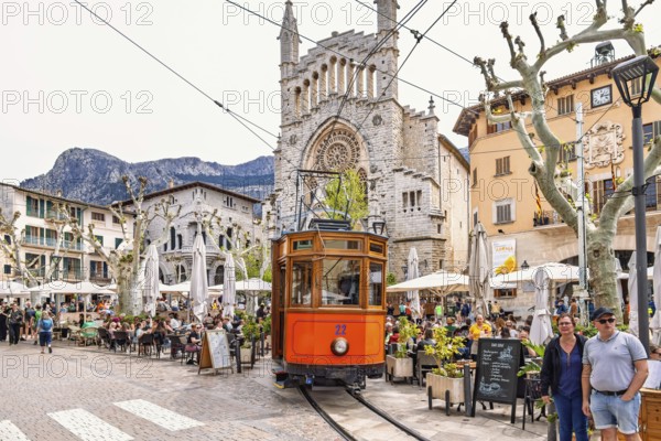 Old vintage train on the city square outside the church between outdoor restaurants and tourists, Sóller, Mallorca, Spain