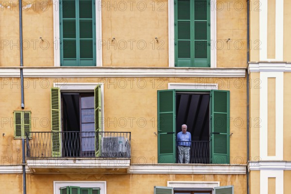 Senior man standing and looking out of an open window in an apartment house, Palma de Mallorca, Mallorca, Spain