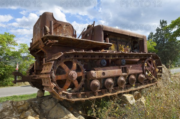 Old, heavily rusted bulldozer for road construction stands abandoned on rocks, industrial relic