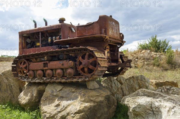 Old, heavily rusted bulldozer for road construction stands abandoned on rocks, industrial relic