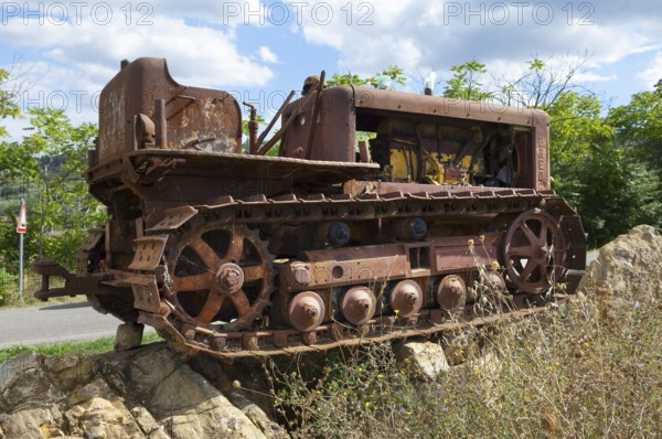 Old, heavily rusted bulldozer for road construction stands abandoned on rocks, industrial relic