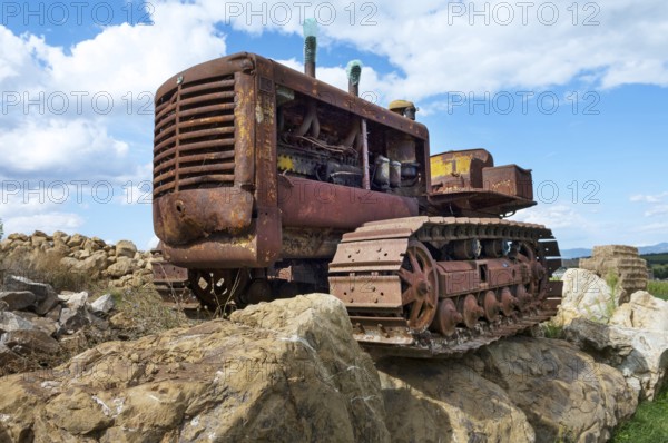 Old, heavily rusted bulldozer for road construction stands abandoned on rocks, industrial relic