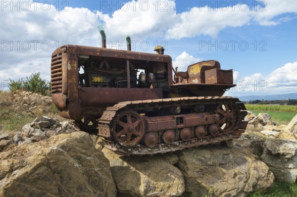 Old, heavily rusted bulldozer for road construction stands abandoned on rocks, industrial relic