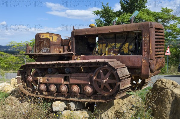 Old, heavily rusted bulldozer for road construction stands abandoned on rocks, industrial relic
