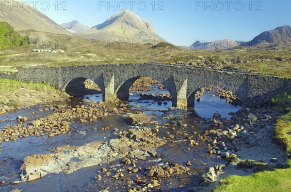 Stone bridge over a shallow river in the middle of a mountain landscape under a clear sky, Slichigan, Isle of Syke, Hebrides, Scotland, United Kingdom