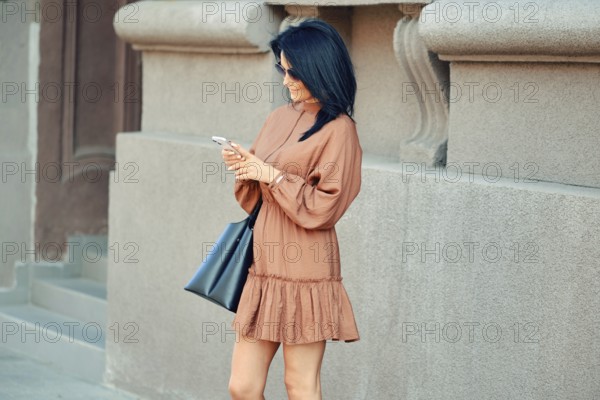 A cheerful woman stands on the street and watching as an online taxi ordered through a smartphone app approaches her