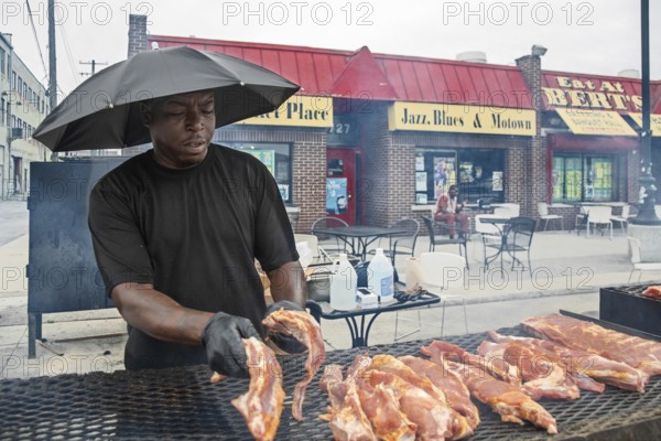 Detroit, Michigan - Wearing an umbrella, a worker places pork on the grill at Bert's Market Place in Eastern Market