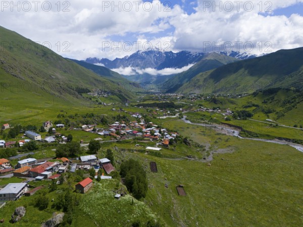 Village in a wide valley between green mountains with clouds in the sky, landscape near Kazbegi, Qasbegi, Stepantsminda, Georgian Military Road, Mtskheta-Mtianeti province, Mount Shani in the background, located in Ingushetia, Russia, High Caucasus, Georgia