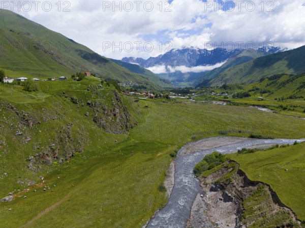 River flowing through green valley, surrounded by mountains and clouds, near a small village, aerial view, Terek River, Kazbegi, Qasbegi, Stepantsminda, Georgian Military Road, Mtskheta-Mtianeti Province, Shani Mountain in the background, located in Ingushetia, Russia, High Caucasus, Georgia