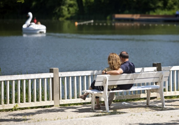 Couple sitting on a wooden bench and looking at the spa pond in the spa gardens, Großer Teich, Bad Nauheim, Hesse, Germany