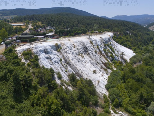 A limestone hillside overlooked by a wooded area under a blue sky, aerial view, Akkaya Travertines, Bolu Province, Turkey