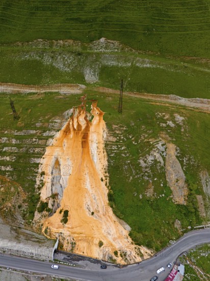 Aerial view of a hill with striking orange rock formation between roads and green landscape, aerial view, Bidara Travertine, Trawertin, Jvari Pass-Trawertin Natural Monument, Cross Pass, Mtskheta-Mtianeti Province, Georgia