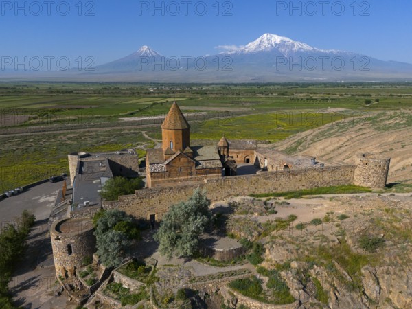 Old church in a green valley with impressive mountain ranges in the background, aerial view, Chor Wirap monastery, Chor Virap, deep dungeon, Ararat and Little Ararat in the background, located in Turkey, Ararat province, Armenia
