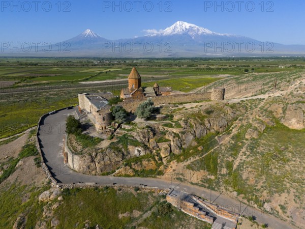 Historical church in front of majestic mountains, embedded in a green landscape with a wide sky, aerial view, monastery Chor Wirap, Chor Virap, deep dungeon, in the background the Ararat and the small Ararat, located in Turkey, Ararat province, Armenia