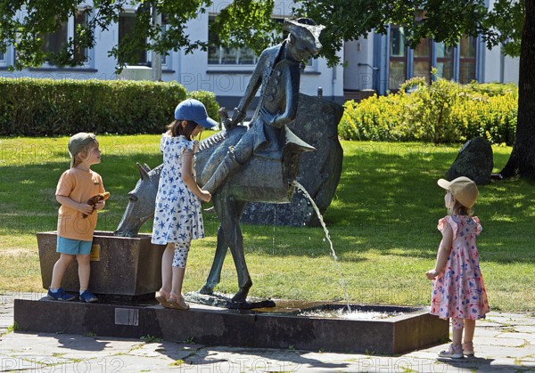 Children at the Münchhausen Fountain by Bruno Schmitz with Münchhausen on the halved horse, Bodenwerder, Weserbergland, Lower Saxony, Germany
