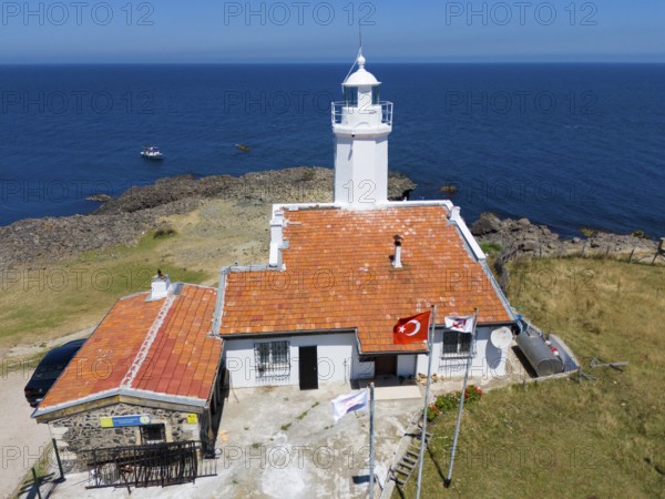 A lighthouse with terracotta roof on a rocky coast with flags and a wide ocean in the background, aerial view, lighthouse, Inceburun, Inceburun is the northernmost point of Anatolia, Sinop province, Turkey