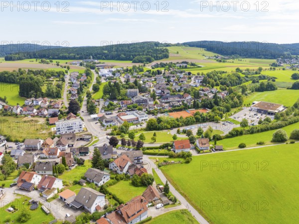 Aerial view of a village in the middle of a green landscape with numerous houses and fields under a blue sky, district of Freudenstadt