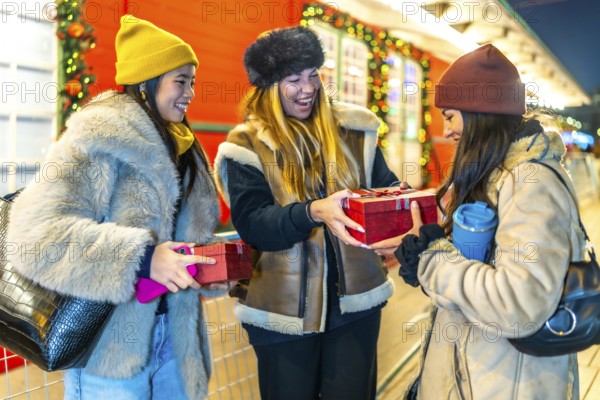 Three joyful women exchanging christmas gifts while enjoying the festive atmosphere of a beautifully decorated night market