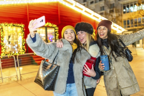 Three happy female friends taking a selfie at a christmas market, enjoying the festive atmosphere and holiday spirit