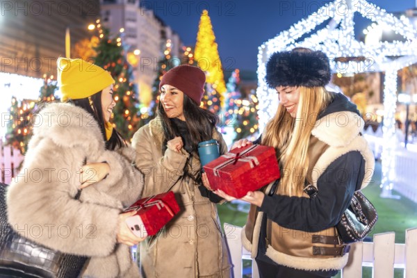 Three joyful women exchanging christmas gifts in a beautifully decorated city square, surrounded by twinkling lights and festive cheer