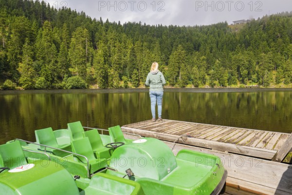Pedal boats and a person on a jetty on the lakeshore, surrounded by forest, Mummelsee, Seebach, Ortenau district, Black Forest, Germany
