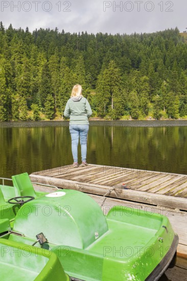 A person stands on a footbridge, looking at a quiet lake in the forest, Mummelsee, Seebach, Ortenau District, Black Forest, Germany