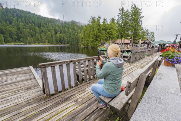 Woman at the lake photographed with her smartphone from a wooden jetty, Mummelsee, Seebach, Ortenau district, Black Forest, Germany