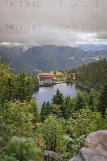 View over a lake with mountains and houses under a cloudy sky, Mummelsee, Seebach, Ortenau District, Black Forest, Germany