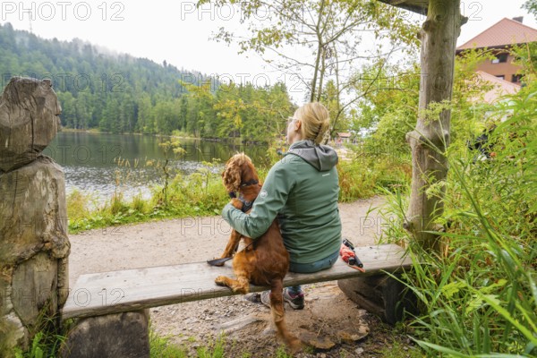 Woman with dog on a bench by the lake in the countryside, relaxed atmosphere in nature, Mummelsee, Seebach, Ortenau district, Black Forest, Germany