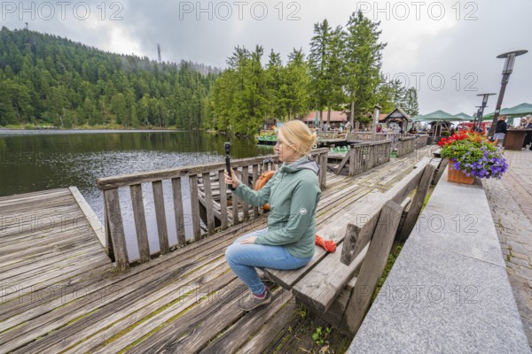 Woman on a wooden footbridge next to a lake with a camera in her hand, Mummelsee, Seebach, Ortenau District, Black Forest, Germany