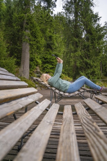 Woman lying relaxed on a wooden bench in a wooded area, Mummelsee, Seebach, Ortenau district, Black Forest, Germany