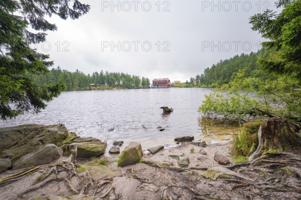 A lake with a rocky shore, a building in the background and surrounded by forest, Mummelsee, Seebach, Ortenau district, Black Forest, Germany