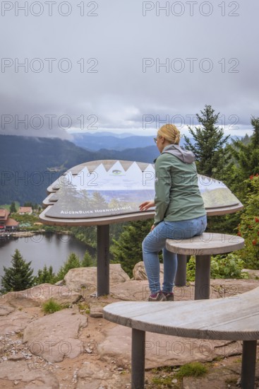 Woman sitting at a viewpoint and looking at the lake and forest landscape in the mountains, Mummelsee, Seebach, Ortenau district, Black Forest, Germany