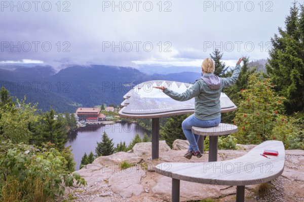 Woman sitting on a wooden bench at a viewpoint, overlooking a lake and mountains, Mummelsee, Seebach, Ortenau District, Black Forest, Germany