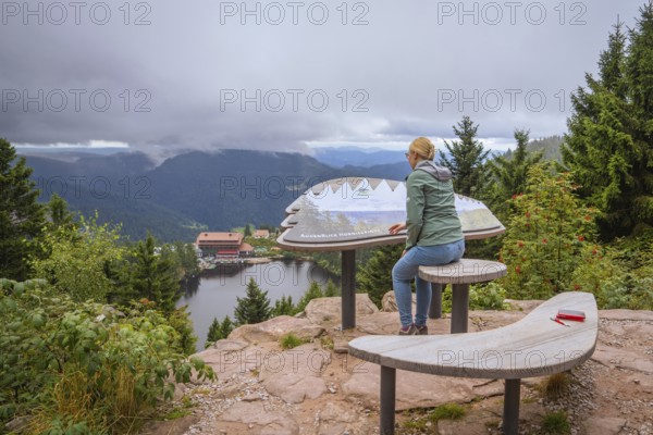 Woman at the panoramic viewpoint with information board, view of lake and forest under clouds, Mummelsee, Seebach, Ortenau district, Black Forest, Germany